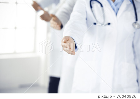 Group of modern doctors standing as a team whole offering helping hand for shaking hand or saving life. Medical help, insurance in health care, best desease treatment and medicine concept 76040926