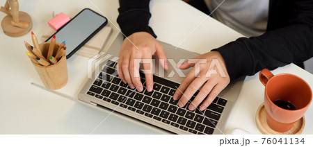 Female hands typing on laptop keyboard on home office desk with stationery, mug and smartphone Female hands typing on laptop keyboard on home office desk with stationery, mug and smartphone 76041134