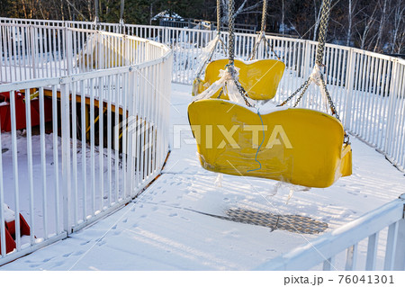 Swinging ride yellow seats covered with snow. Winter amusement park, low season. Unused carousel, cold time. 76041301