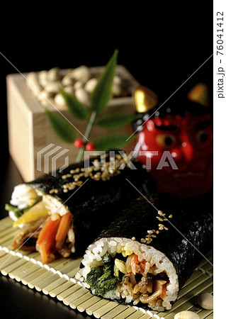 韓国風太巻きと鬼のお面と大豆を黒背景で撮影 76041412