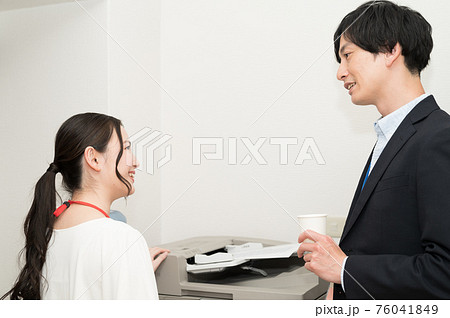 コピー機の前で水を飲みながら雑談をする男女の社員 76041849