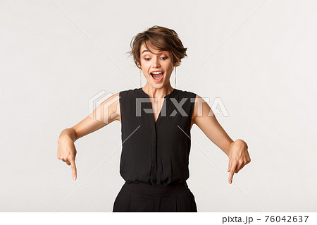 Amazed and happy young woman looking, pointing fingers down at banner, standing white background 76042637
