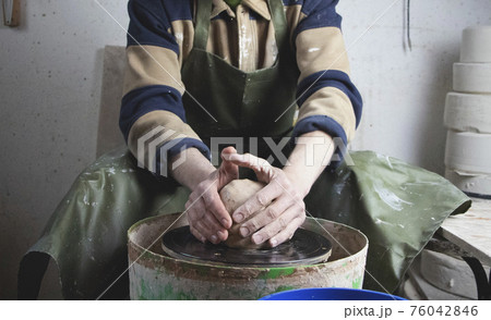 Hands of a potter on a pottery wheel close-up. Old traditional art, handmade, clay and ceramic production. Pottery workshop in subdued soft light 76042846