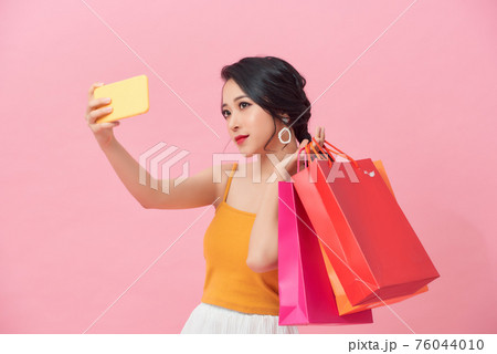 Portrait smiling woman holding packages bags with purchases after shopping doing selfie shot on mobile phone Portrait smiling woman holding packages bags with purchases after shopping doing selfie shot on mobile phone 76044010