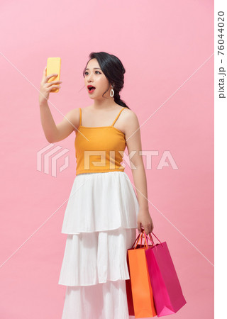 Surprised young woman with mobile phone and shopping bags on color background 76044020