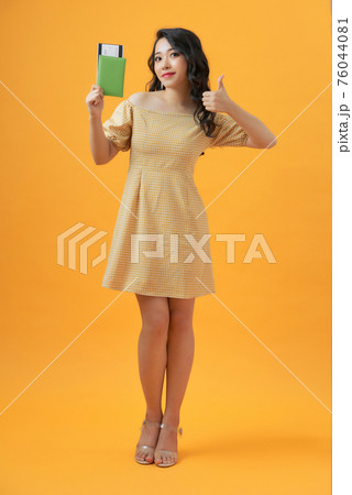 Smiling young woman isolated on yellow background. Hold passport tickets, showing thumb up 76044081