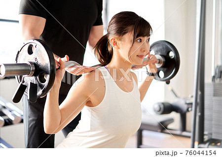 トレーナーの補助付きでバーベルスクワットをするアジア人女性 76044154