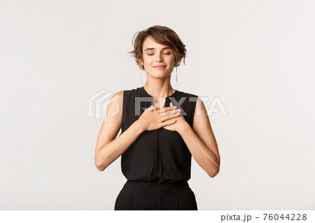 Image of nostalgic happy young woman close eyes and holding hands on heart while remember something, smiling pleased, white background 76044228