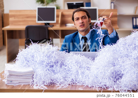 Young male employee and a lot of cut papers in the office Young male employee and a lot of cut papers in the office 76044551