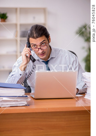 Young male employee unhappy with excessive work in the office Young male employee unhappy with excessive work in the office 76045828