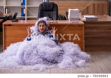 Young male employee and a lot of cut papers in the office Young male employee and a lot of cut papers in the office 76046663