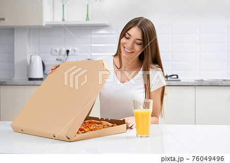 Smiling woman opening box with pizza in kitchen. 76049496