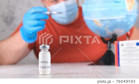 vial with a vaccine against the coronavirus, in the background a man is vaccinating the planet, the vial with a vaccine against the coronavirus, in the background a man is vaccinating the planet, the 76049593