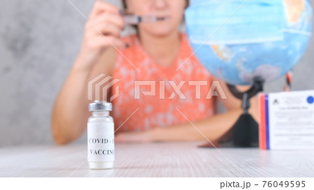 vial with a vaccine against coronavirus, in the background, a woman is vaccinating the planet, the vial with a vaccine against coronavirus, in the background, a woman is vaccinating the planet, the 76049595