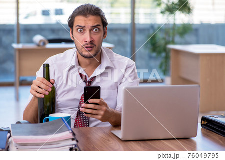 Young male alcohol addicted employee working in the office Young male alcohol addicted employee working in the office 76049795