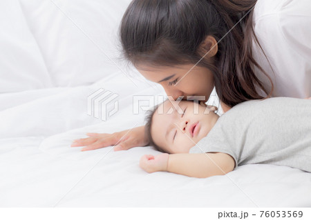 Young asian mother kiss cheek of little baby girl with tender on bed in the bedroom. Young asian mother kiss cheek of little baby girl with tender on bed in the bedroom. 76053569
