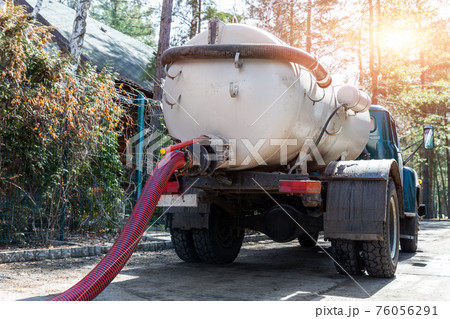 Close-up pipe hose of sewage truck car engine emptying home sewerage tank. Septic cleaning vacuum service and maintenance suburban countryside home. Suction vehicle cleaner machine pumping drainage Close-up pipe hose of sewage truck car engine emptying home sewerage tank. Septic cleaning vacuum service and maintenance suburban countryside home. Suction vehicle cleaner machine pumping drainage 76056291