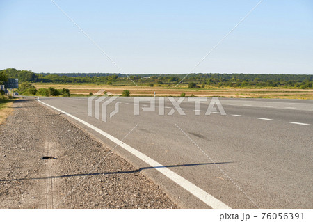 soft focus asphalt road surface with white markings close-up from the low shot. blured country road and field with forest in summer. High quality photo. Travel, tehnology, nature comcept. 76056391