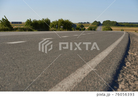 soft focus asphalt road surface with white markings close-up from the low shot. blured country road and field with forest in summer. High quality photo. Travel, tehnology, nature comcept. 76056393