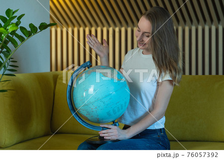 Young woman while sitting on sofa at home holding a world globe choose a route of travel. Young woman while sitting on sofa at home holding a world globe choose a route of travel. 76057392