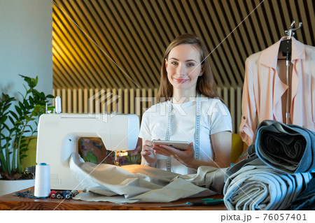 Young female seamstress makes notes about clothing measurements on a notebook in a sewing workshop. Young female seamstress makes notes about clothing measurements on a notebook in a sewing workshop. 76057401