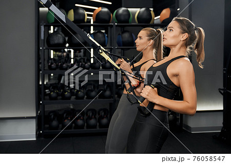Cute women doing workout with trx system in gym. 76058547