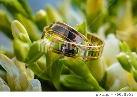 two gold wedding rings lie on the flowers of a beautiful bouquet 76058955