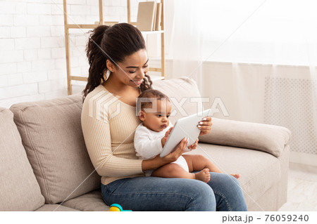 African Mom Holding Baby Watching Cartoons On Tablet At Home African Mom Holding Baby Watching Cartoons On Tablet At Home 76059240