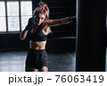 Athletic fit female boxer exercising punches with boxing bag in gym during kickboxing and self defense intensive workout 76063419