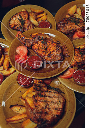 Cast iron plate with sliced grilled rib-eye steak on table with yellow potato wedges and oil in saucer over table with copy space. Cast iron plate with sliced grilled rib-eye steak on table with yellow potato wedges and oil in saucer over table with copy space. 76063818