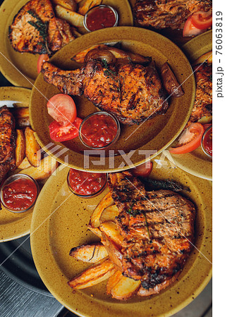 Cast iron plate with sliced grilled rib-eye steak on table with yellow potato wedges and oil in saucer over table with copy space. 76063819
