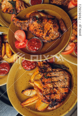 Cast iron plate with sliced grilled rib-eye steak on table with yellow potato wedges and oil in saucer over table with copy space. 76063821