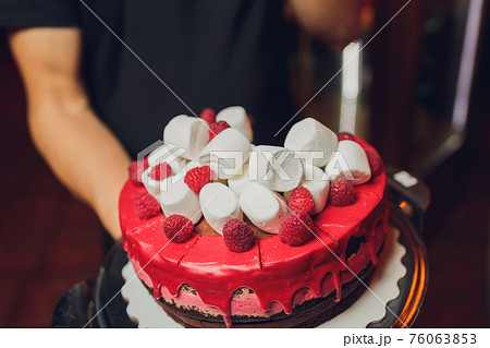 Happy Canada Day celebration cake with flags, marshmallow and candy decorations on a red cake stand on a white table against a red background. 76063853