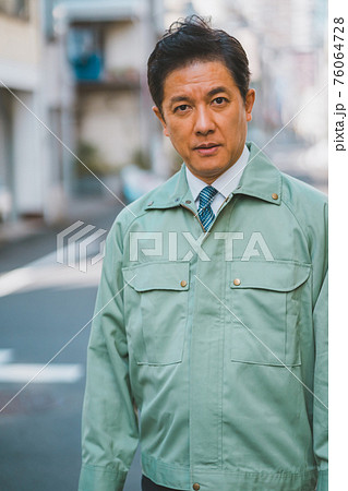 作業服にネクタイ姿の50代男性が街でカメラ目線 76064728