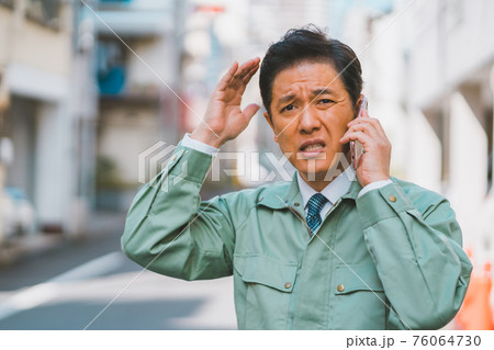 作業服にネクタイ姿の男性が電話で怒られる 76064730