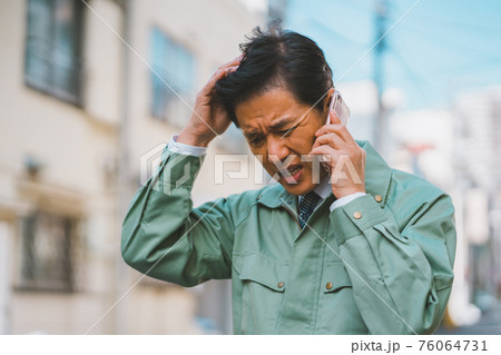 作業服にネクタイ姿の男性が電話で怒られる 76064731