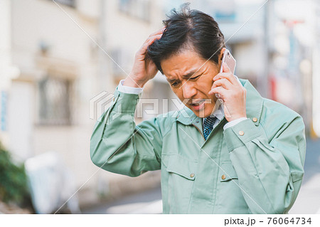作業服にネクタイ姿の男性が電話で怒られる 作業服にネクタイ姿の男性が電話で怒られる 76064734