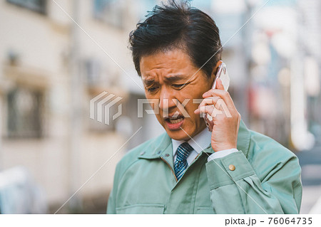 作業服にネクタイ姿の男性が電話で怒られる 作業服にネクタイ姿の男性が電話で怒られる 76064735