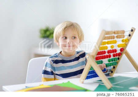 Elementary student boy doing homework at home. Child learning to count, solves arithmetic examples, using abacus. Math tutorial. Preparing preschooler baby for school. Education Elementary student boy doing homework at home. Child learning to count, solves arithmetic examples, using abacus. Math tutorial. Preparing preschooler baby for school. Education 76065251