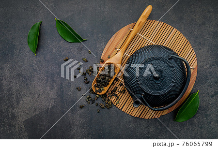 Black cast iron tea pot with herbal tea set up on dark stone background. 76065799