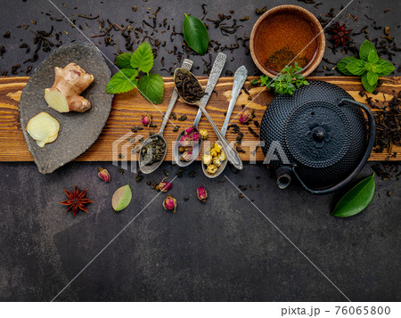 Black cast iron tea pot with herbal tea set up on dark stone background. 76065800