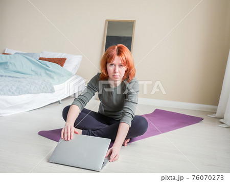 Red hair woman sitting cross-legged on yoga mat Red hair woman sitting cross-legged on yoga mat 76070273