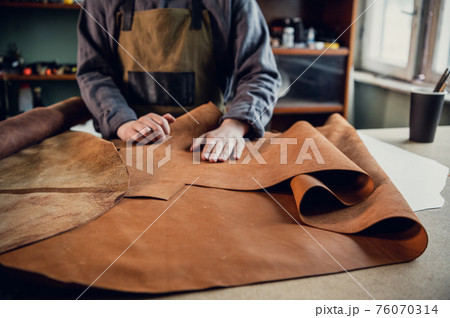 Before making shoes out of leather, a young guy lays them out on the table in the workshop 76070314