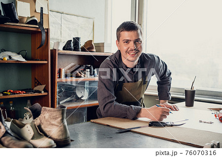 The first stage in the production of shoes is to make an exact pattern from paper, a young shoemaker in uniform at work The first stage in the production of shoes is to make an exact pattern from paper, a young shoemaker in uniform at work 76070316