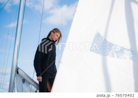 A young blonde athlete on a yacht against a blue sky, a mast and a white sail. A young blonde athlete on a yacht against a blue sky, a mast and a white sail. 76070402