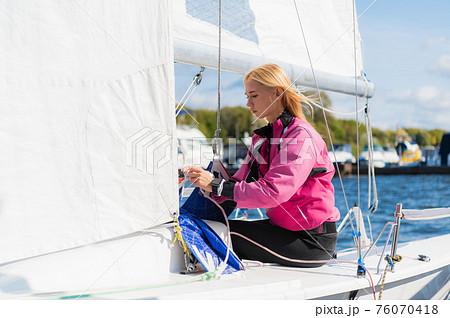 Young athletic girl in sports clothes on a yacht in the dock is ready for a sailing regatta. 76070418