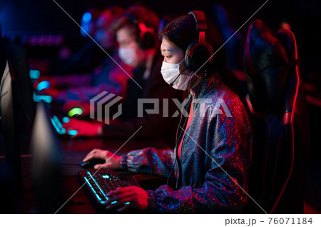 An online strategy tournament for esports players in the cyber games arena. A professional team of cyber-athletes competes with another crew, asian woman in a medical mask An online strategy tournament for esports players in the cyber games arena. A professional team of cyber-athletes competes with another crew, asian woman in a medical mask 76071184