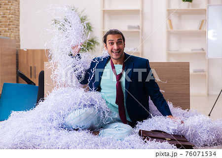 Young male employee and a lot of cut papers in the office Young male employee and a lot of cut papers in the office 76071534
