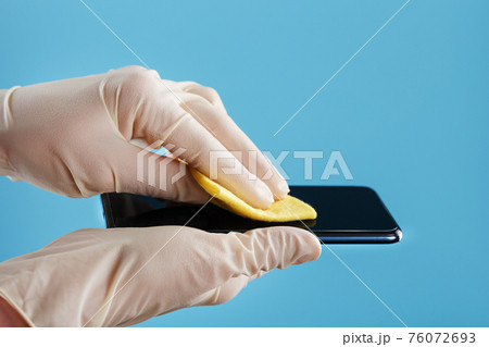 Disinfection of the smartphone with a yellow napkin with antibacterial impregnation in hand gloves. Disinfection of the smartphone with a yellow napkin with antibacterial impregnation in hand gloves. 76072693