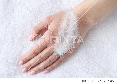 Soft white feather lying on woman hand closeup 76073465